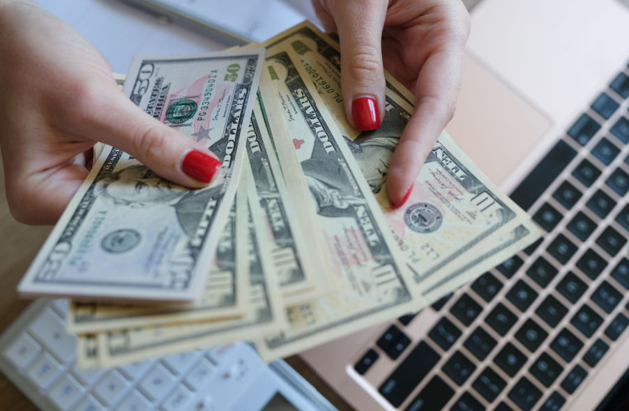 womans hand counting dollar bills for investing in gold ira